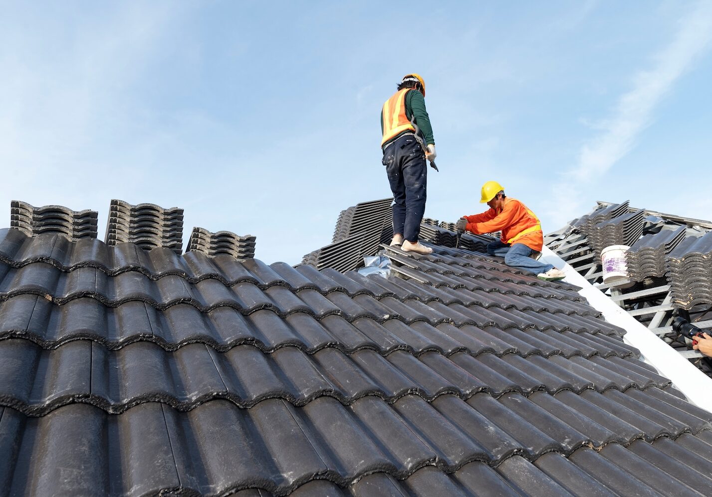 Builders in work clothes install new roofing tools, roofing tools, electric drill and use them on new wooden roofs with metal sheets