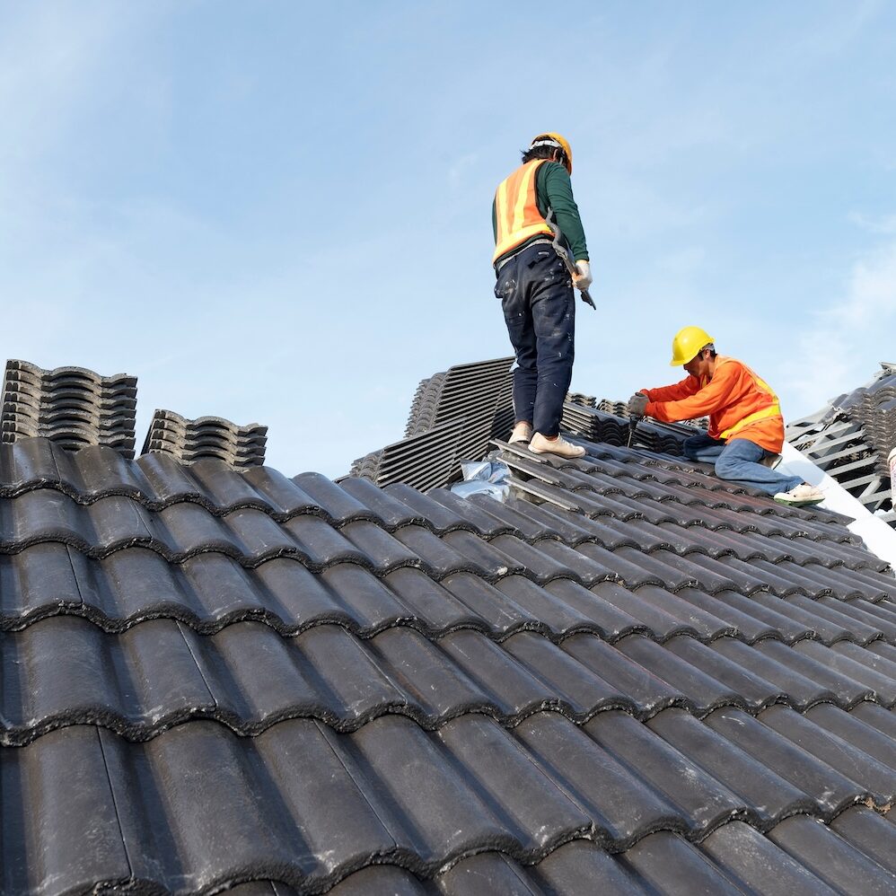 Builders in work clothes install new roofing tools, roofing tools, electric drill and use them on new wooden roofs with metal sheets