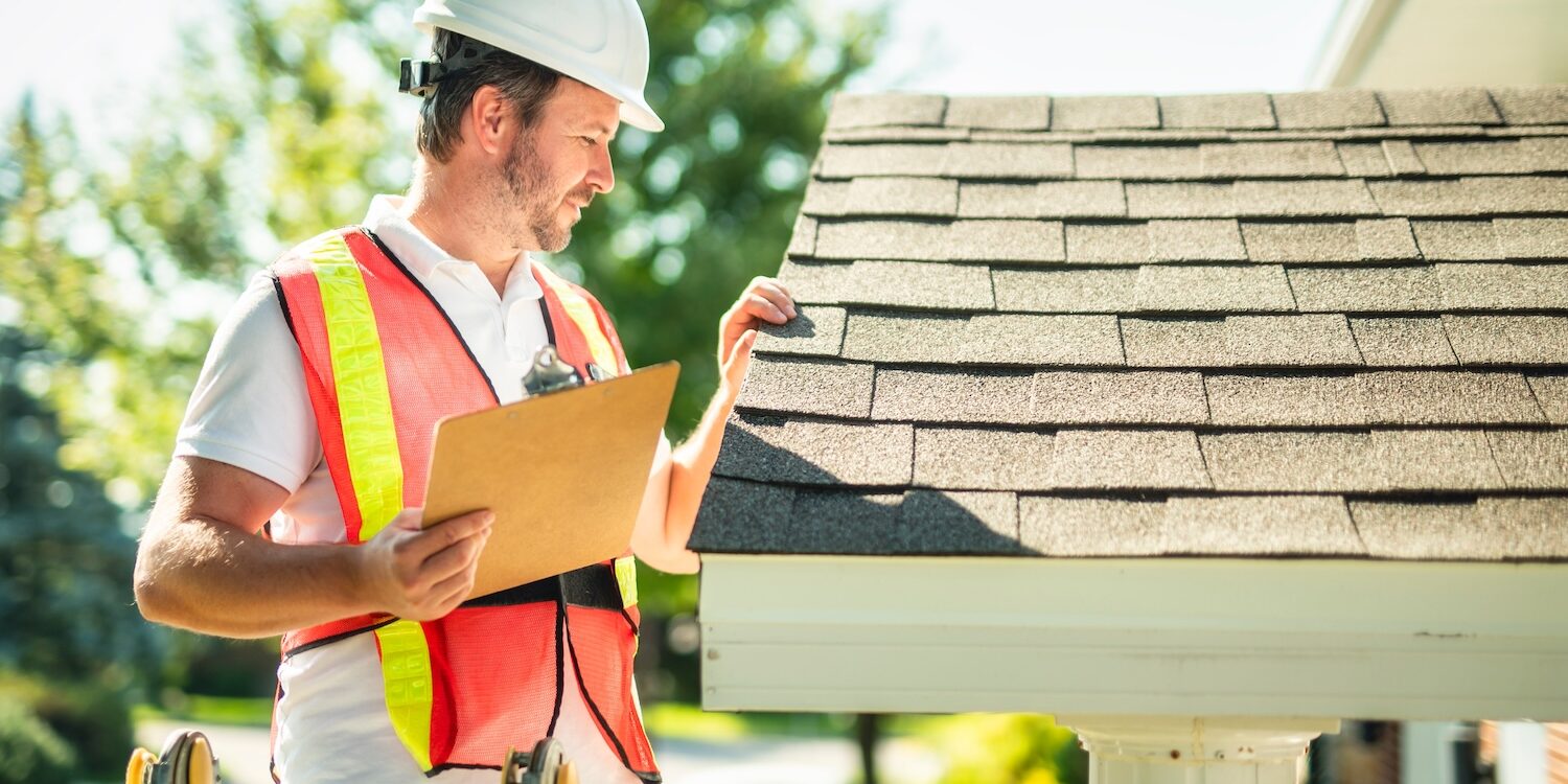 A man with hard hat standing on steps inspecting house roof
