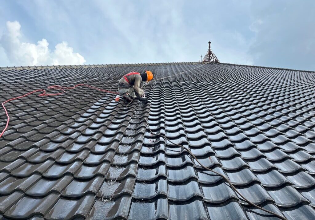 a worker cleans a tiled roof manually using brush equipment and water