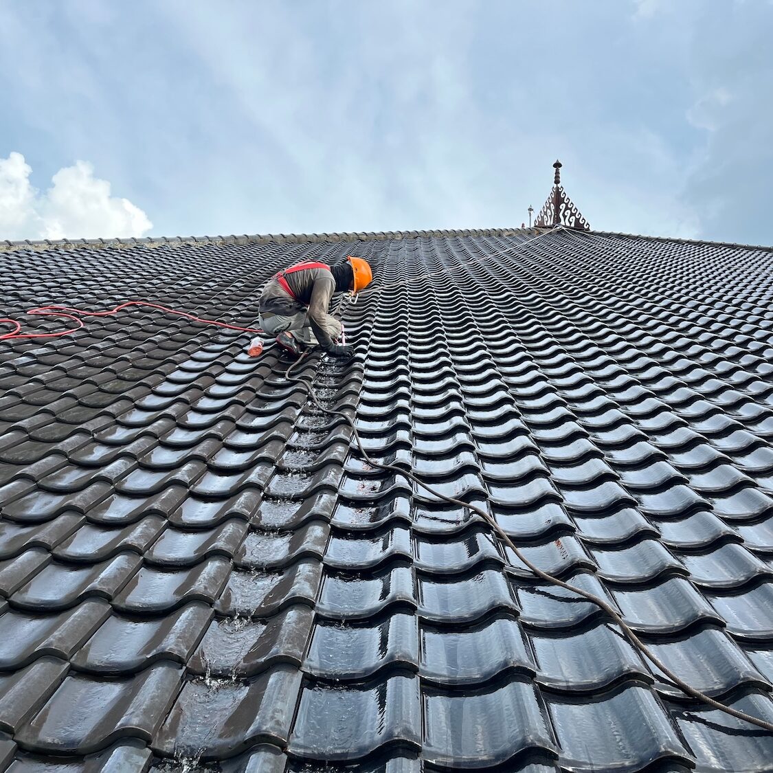 a worker cleans a tiled roof manually using brush equipment and water