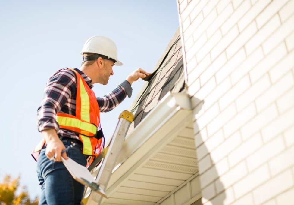 A man with hard hat standing on steps inspecting house roof