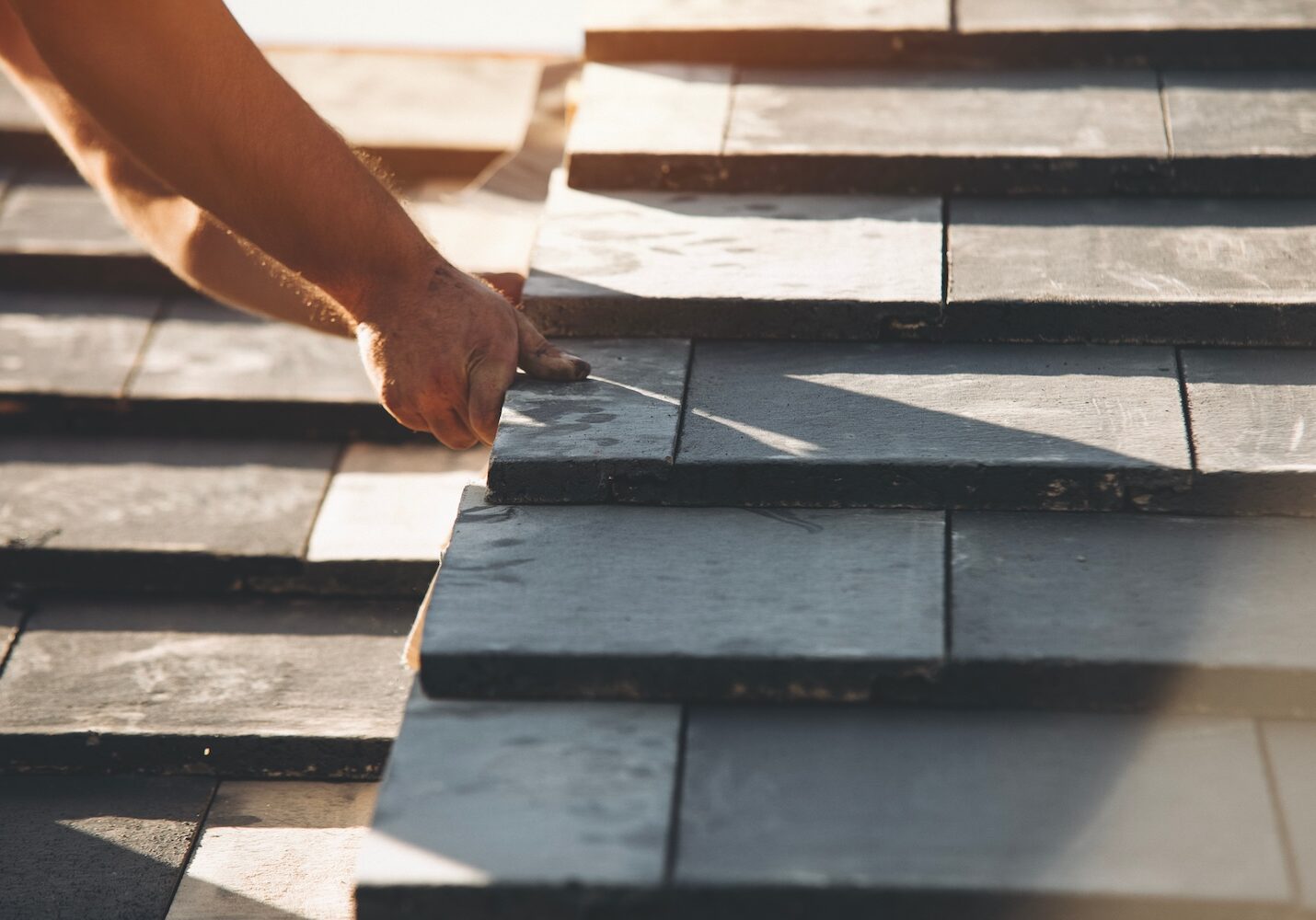 Roofing project in progress as a worker lays slate tiles during late afternoon sunlight