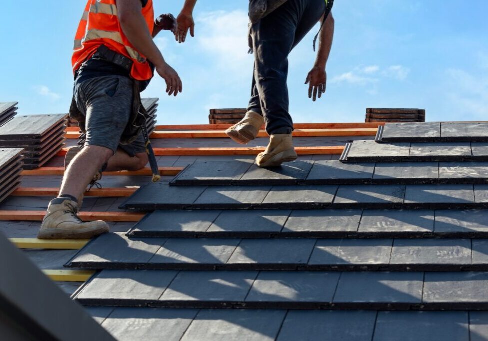 Roofers install slate tiles on a sunny day at a construction site in a suburban area