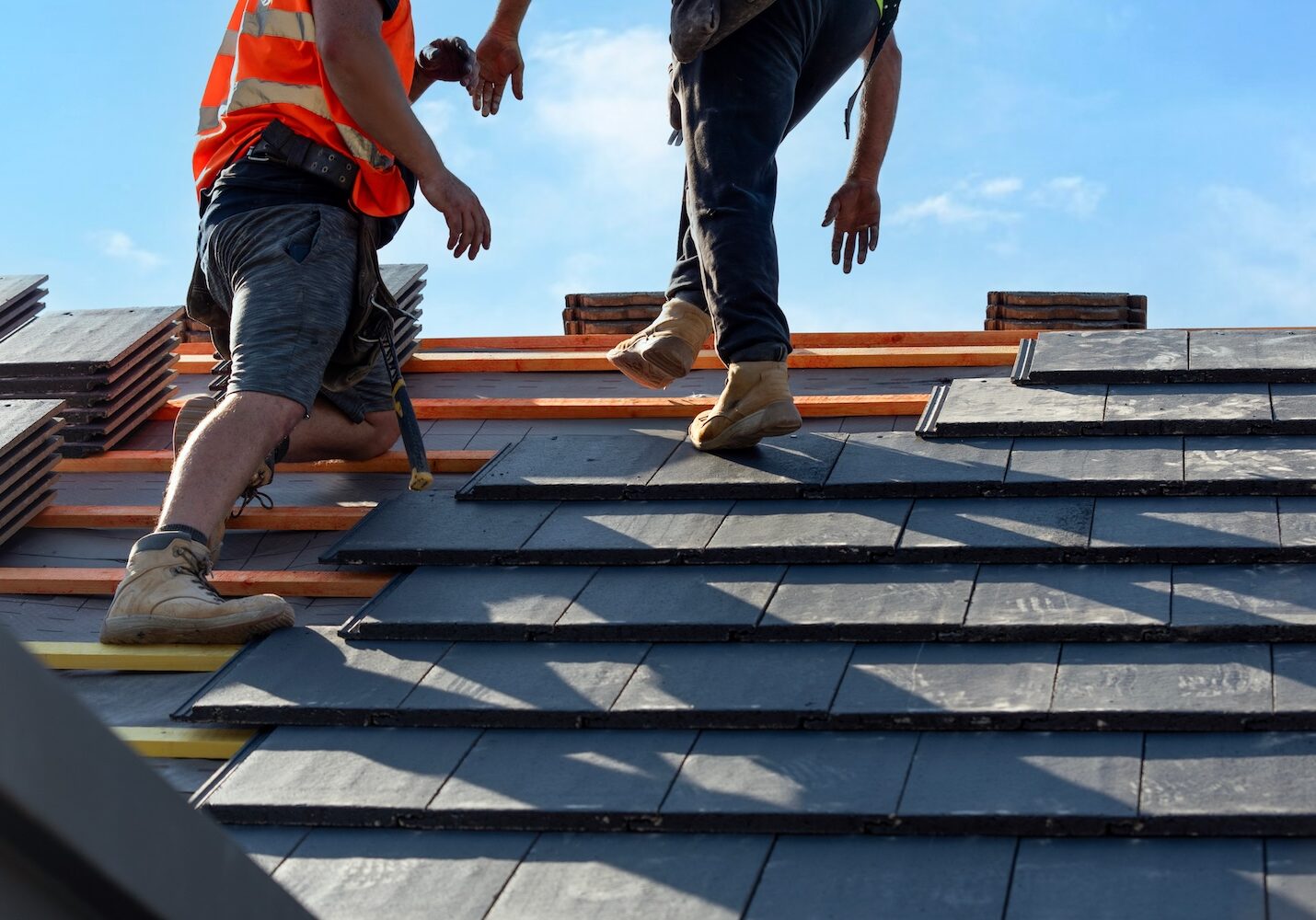 Roofers install slate tiles on a sunny day at a construction site in a suburban area
